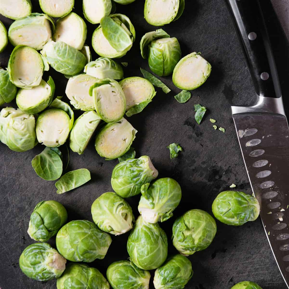 Halved Brussels sprouts on a cutting board next to a chef knife
