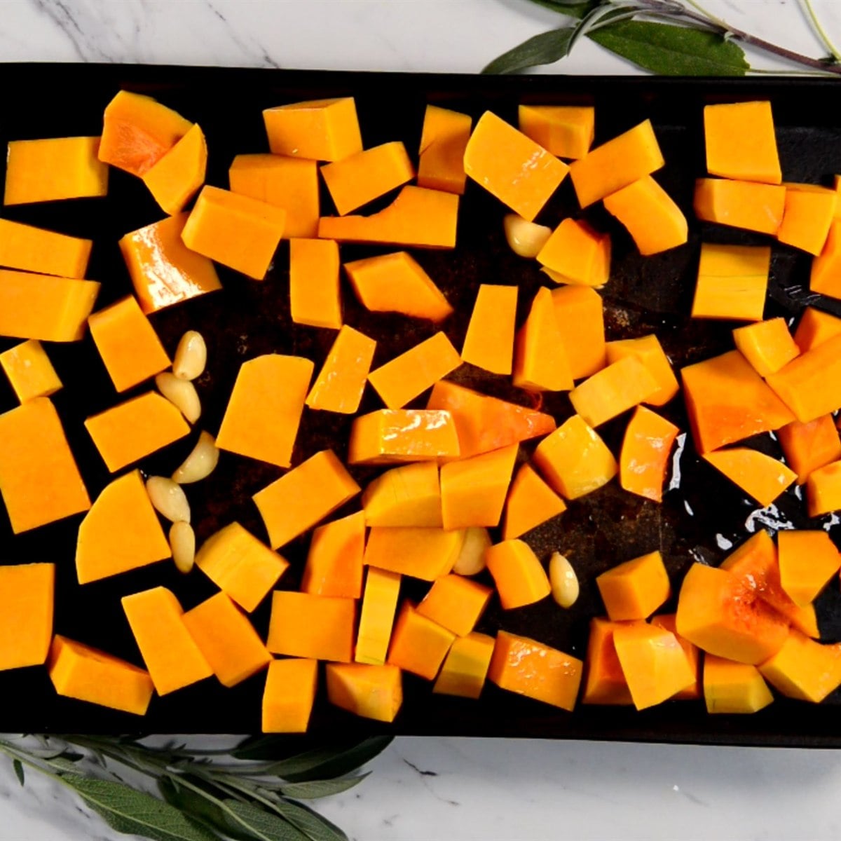 cubed butternut squash and whole garlic cloves on a baking sheet, ready to roast