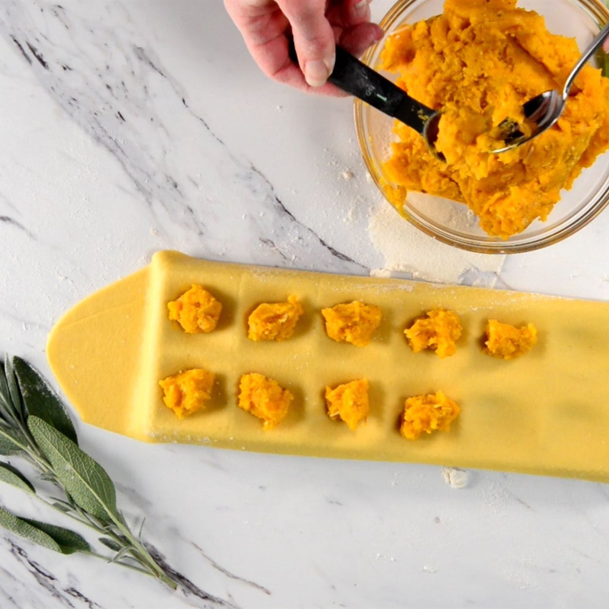 spooning butternut squash filling onto a sheet of pasta dough in a ravioli mold