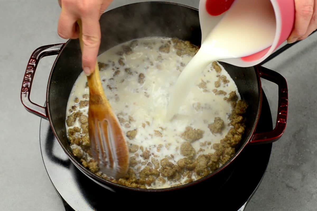 Adding milk to crumbly cooked breakfast sausage coated in roux to make a creamy sausage gravy for biscuits and gravy.