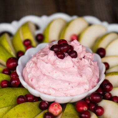 Cranberry fruit dip in a white bowl on a platter of sliced pears and fresh cranberries.