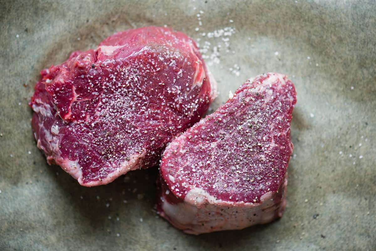 two raw filet mignon steaks seasoned with kosher salt and pepper
