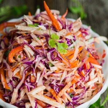 Jicama slaw with red cabbage, carrots and cilantro piled in a white bowl on a wooden table