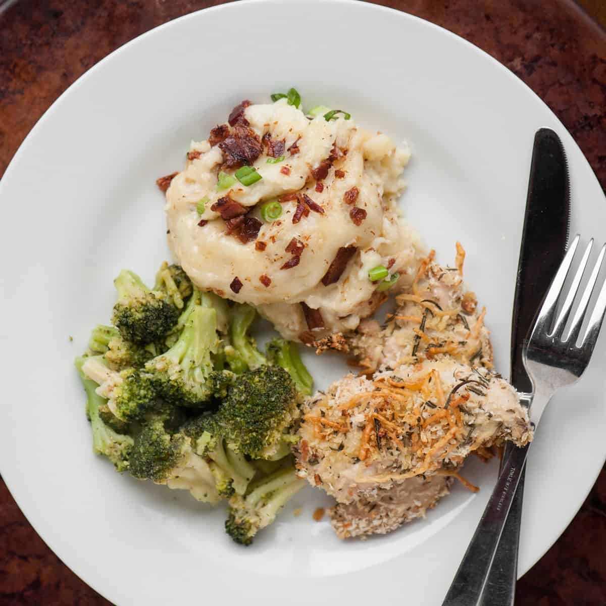 Dinner plate with loaded cheesy mashed potato casserole, broccoli and a breaded chicken breast.