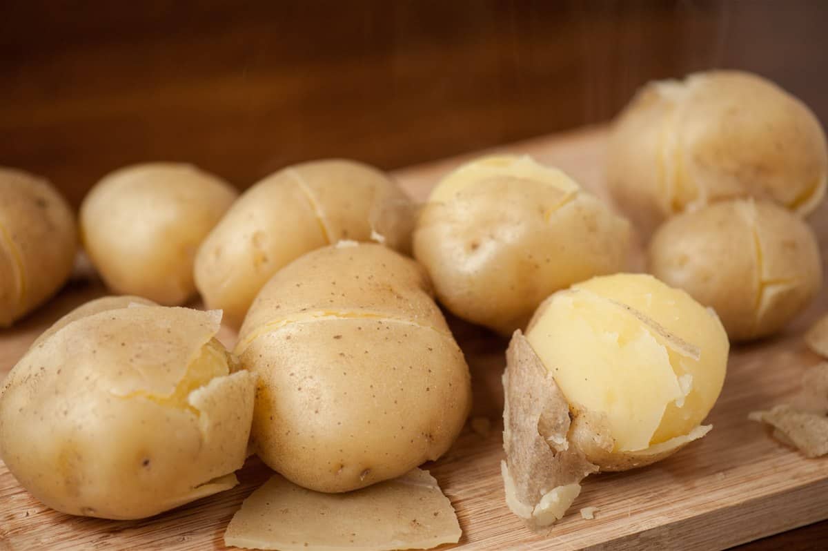 Boiled whole golden potatoes on a cutting board with their skins split and slipping off.