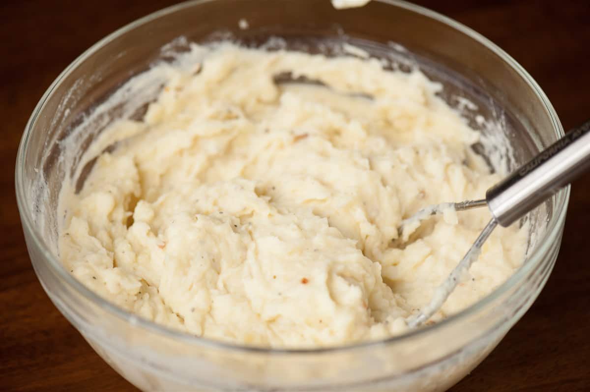 Creamy mashed potatoes with cheese and sour cream in a glass bowl with a masher.