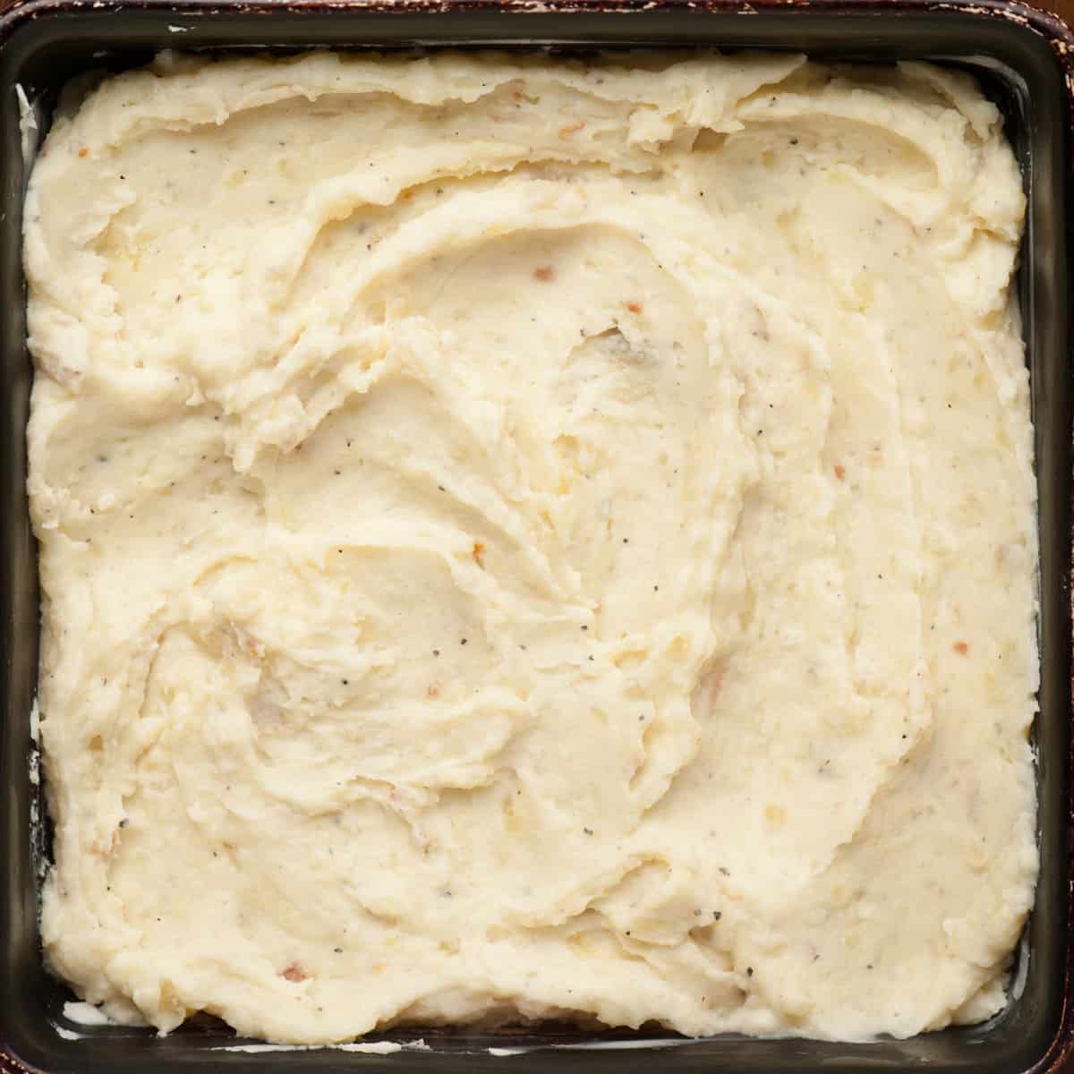 Cheesy mashed potatoes spread evenly in a square baking dish.