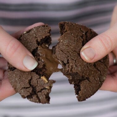 Hands breaking a Nutella stuffed chocolate cookie in half to show the melted Nutella center