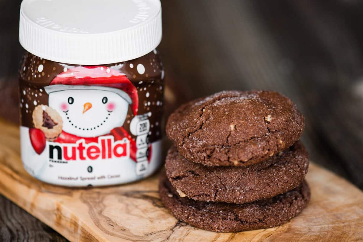 Stack of sugar-coated chocolate hazelnut cookies next to a holiday jar of Nutella