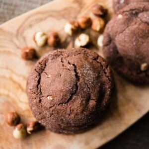 Sugar-crusted Nutella stuffed chocolate cookie on an olive wood board with whole hazelnuts