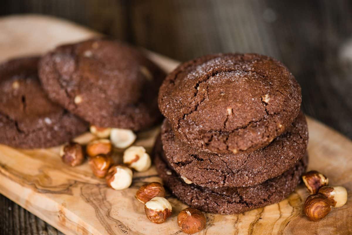 Stacked chocolate hazelnut cookies on an olive wood board with whole hazelnuts