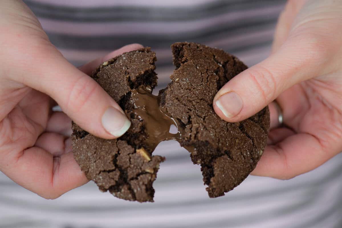 Hands breaking a Nutella stuffed chocolate cookie in half to show the melted Nutella center