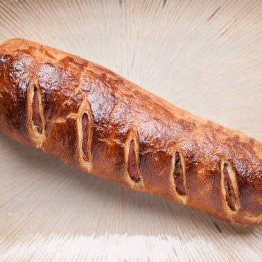 Whole baked pork Wellington with a shiny golden puff pastry crust and diagonal slits on top