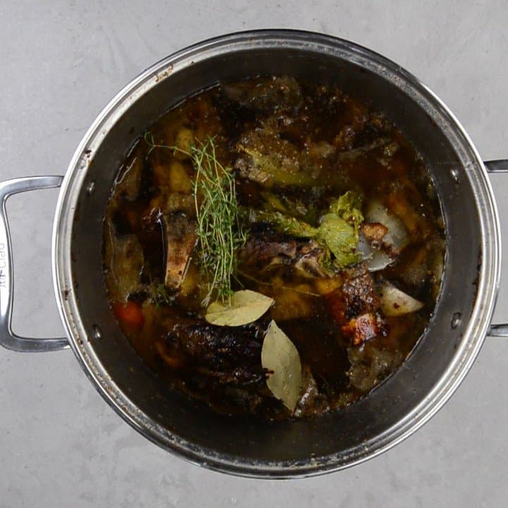 roasted bones, vegetables, thyme and bay leaves in a stockpot of water.