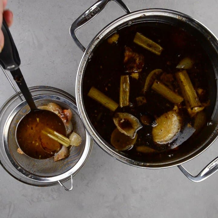 ladling beef broth through a strainer.