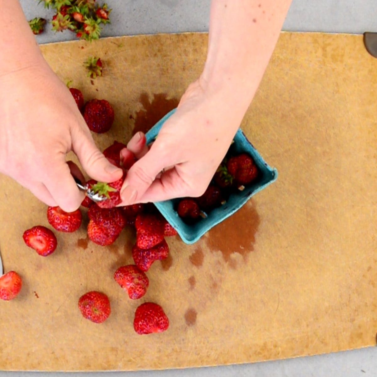 removing the stems from fresh strawberries on a cutting board