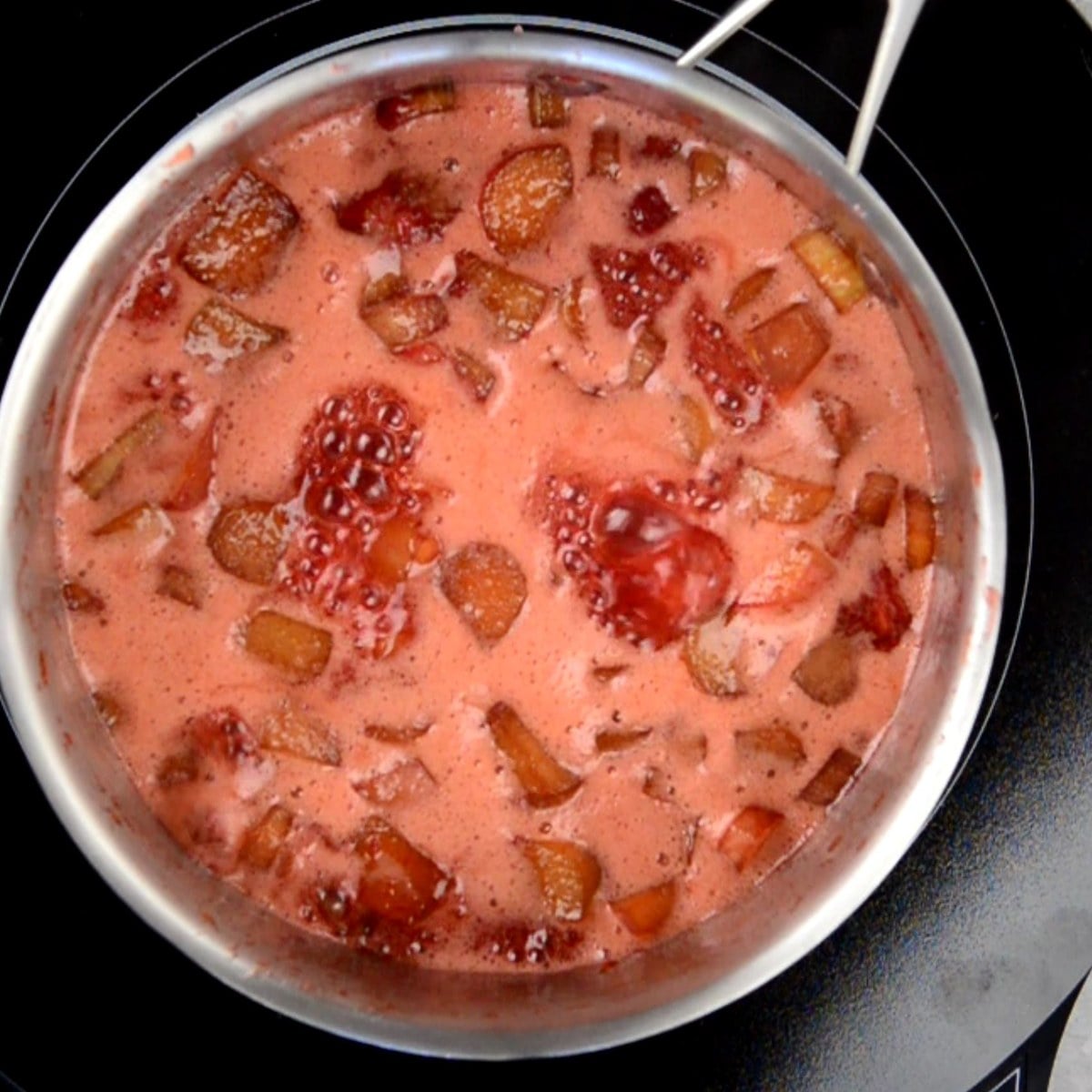strawberry rhubarb jam starting to bubble in a saucepan