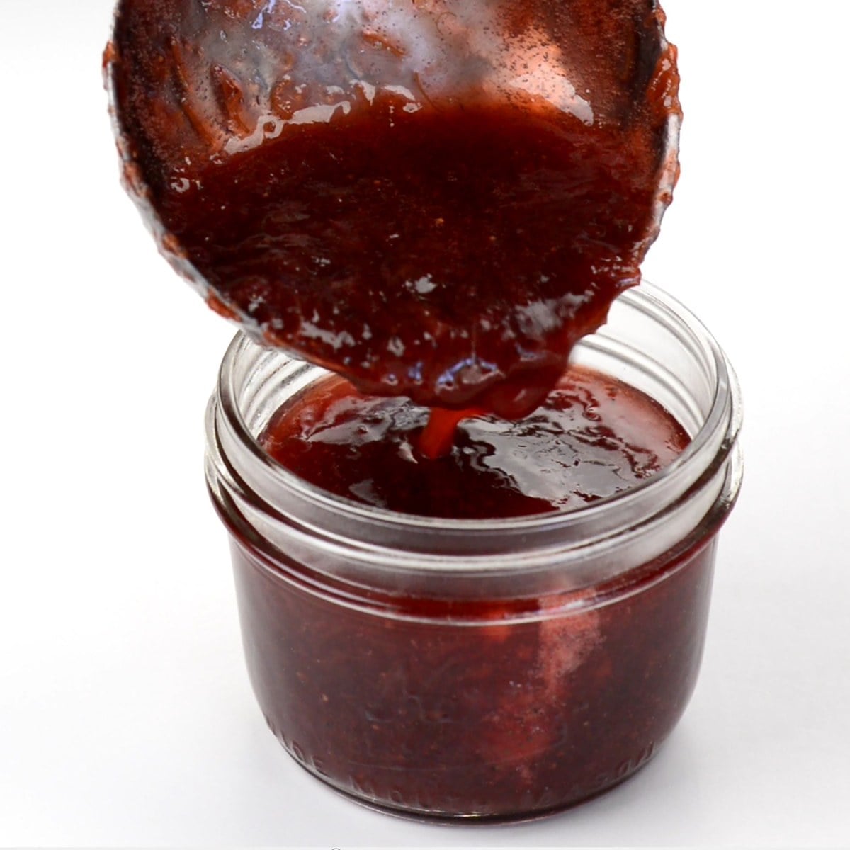 pouring strawberry rhubarb jam into a small mason jar