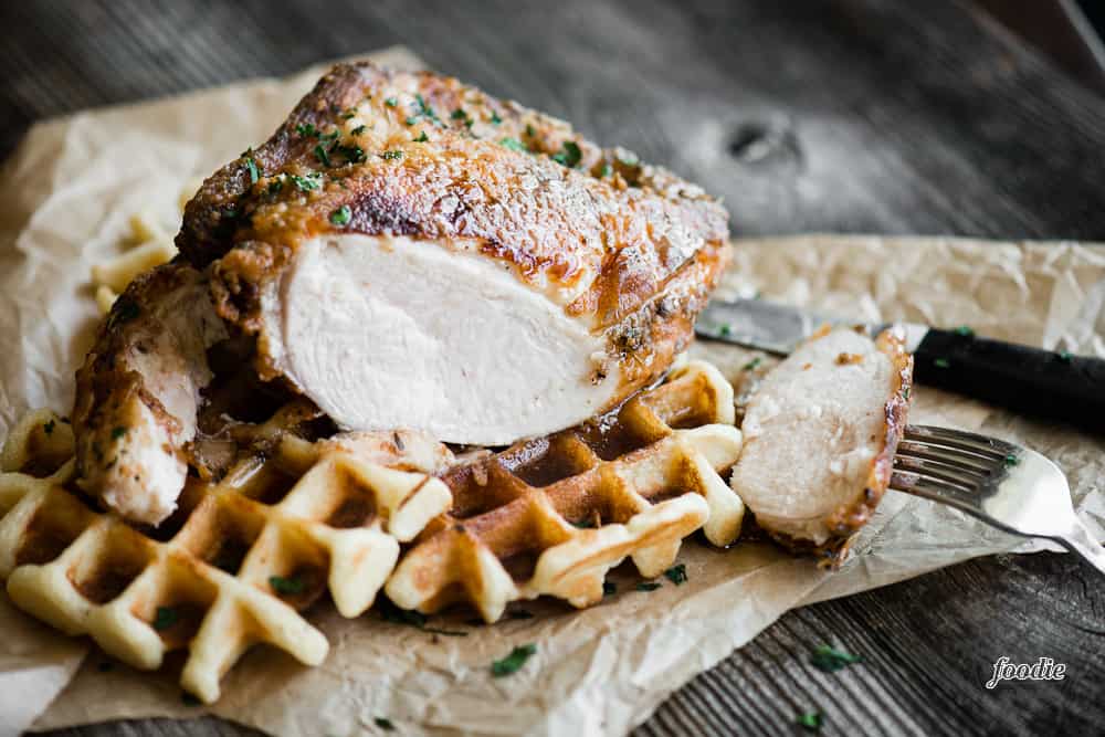 fried chicken breast with bite cut off on top of waffle