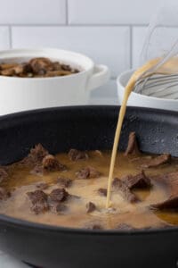 Pouring gravy over sliced beef sirloin in pan.