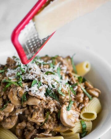 grating parmesan cheese over bowl of sausage mushroom rigatoni