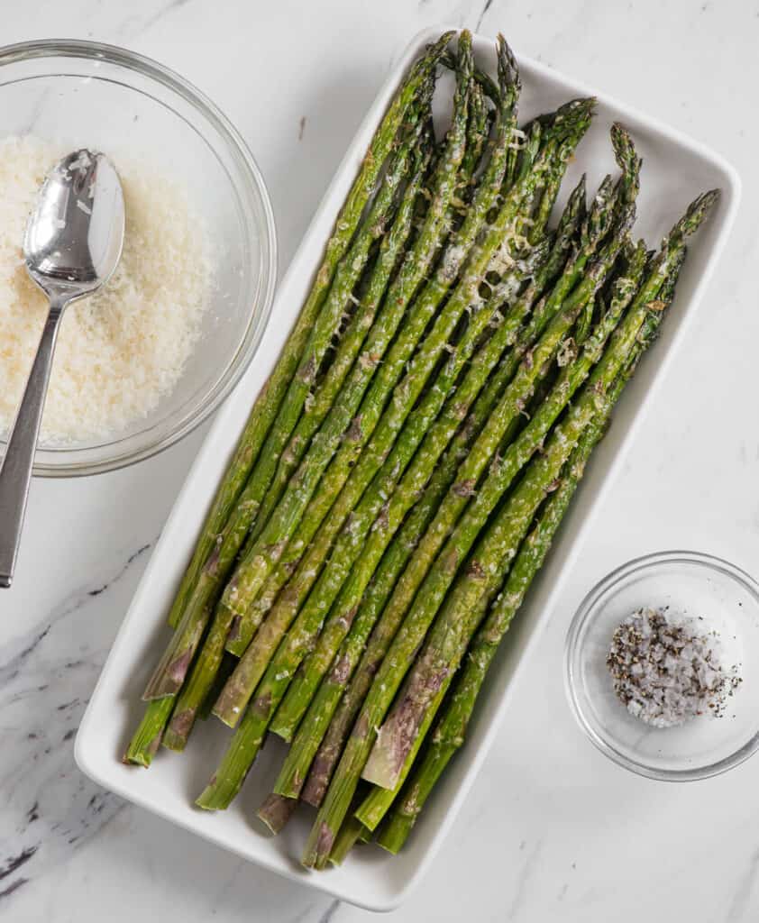 asparagus spears on rectangular platter with parmesan cheese in bowl