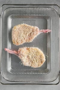 two breaded pork chops in air fryer basket prior to cooking