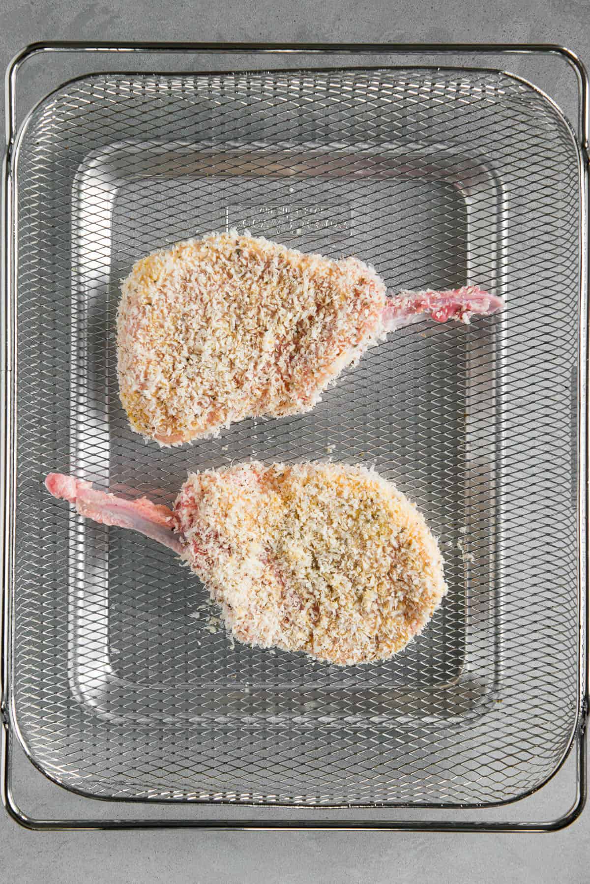 two breaded pork chops in air fryer basket prior to cooking