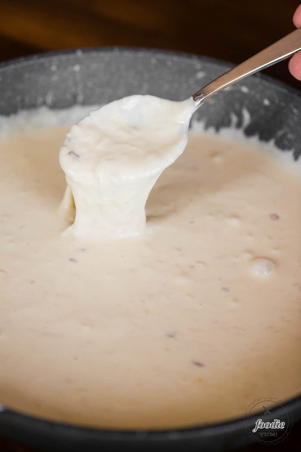 Homemade alfredo sauce on spoon and in pan