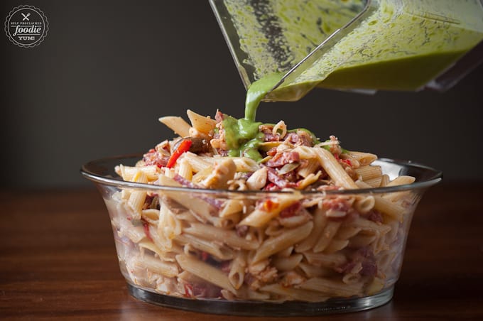 pouring green dressing on pasta salad