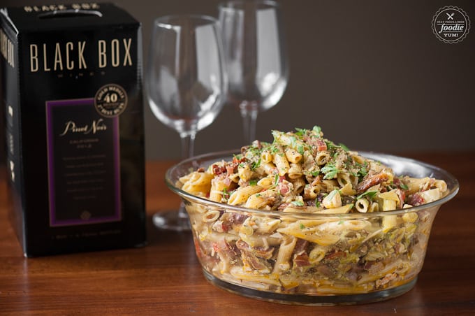 a bowl of antipasto pasta salad with wine glasses and box of wine