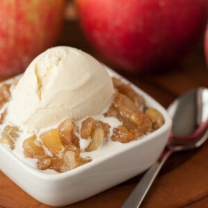 Serving of apple brown betty with vanilla ice cream on top and apples in the background.