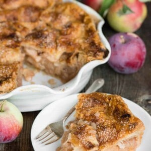 slice of apple pie on plate with whole pie and apples in background