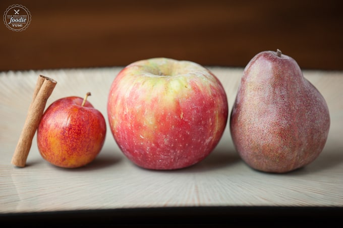 An apple, plum, and pear sitting on top of a wooden table