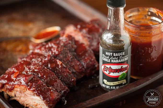 bottle of hot sauce next to sliced pork ribs