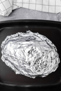 Wrapping an entire ham in foil to bake it.