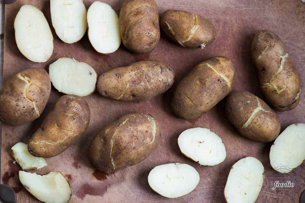 lots of baked potatoes on cutting board, some cut in half