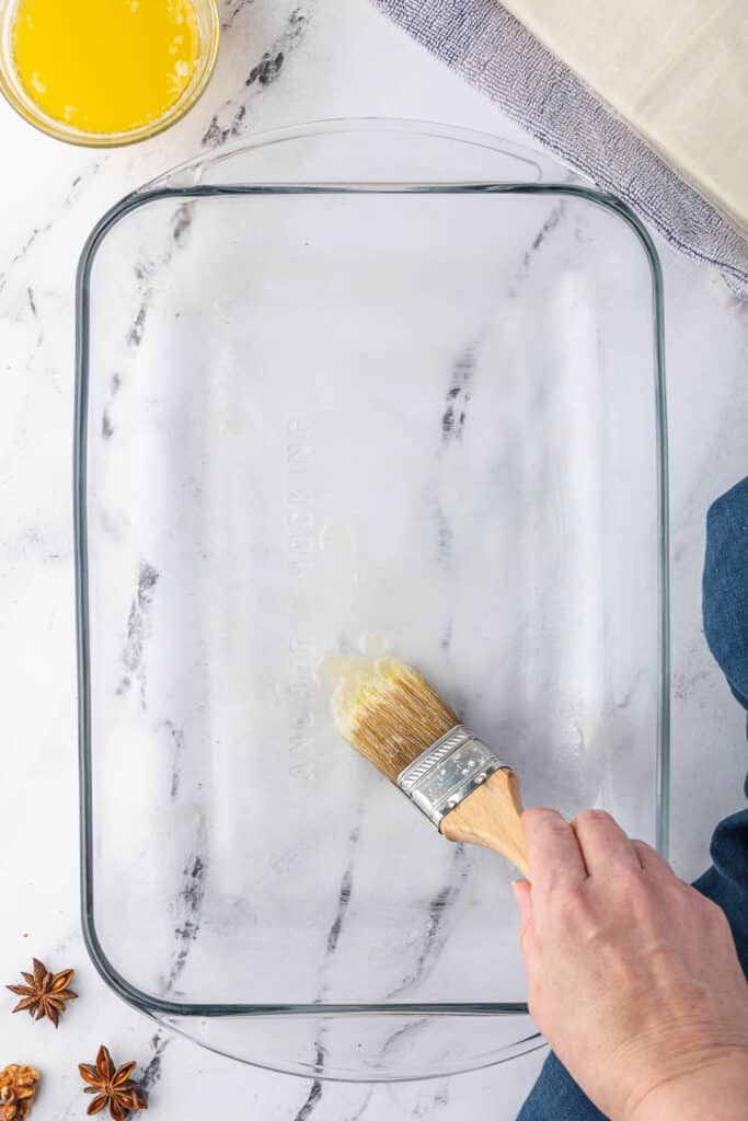 painting melted butter into baking dish