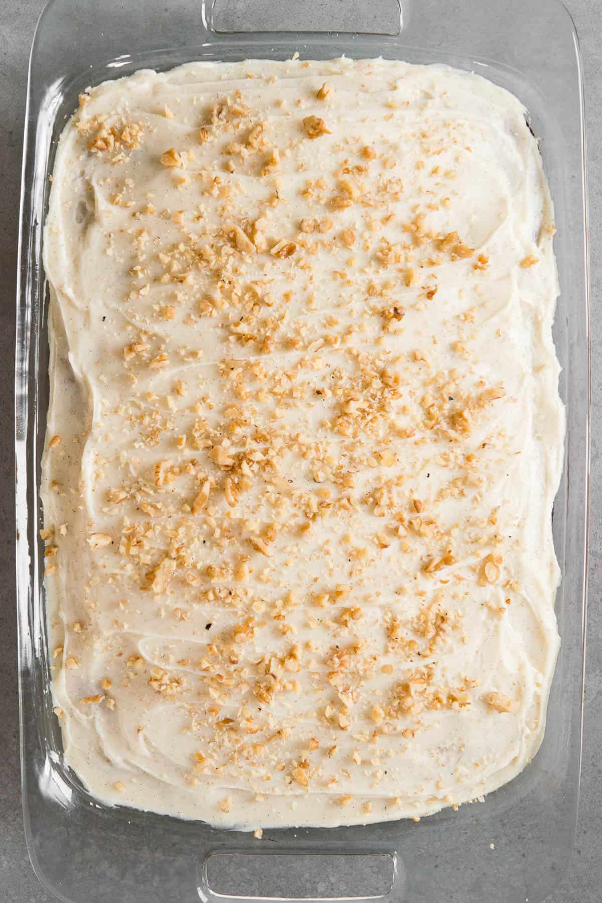 single layer banana cake in glass baking dish covered in frosting and chopped walnuts.