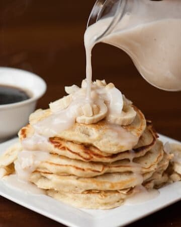 pouring sweet coconut syrup on stack of banana pancakes