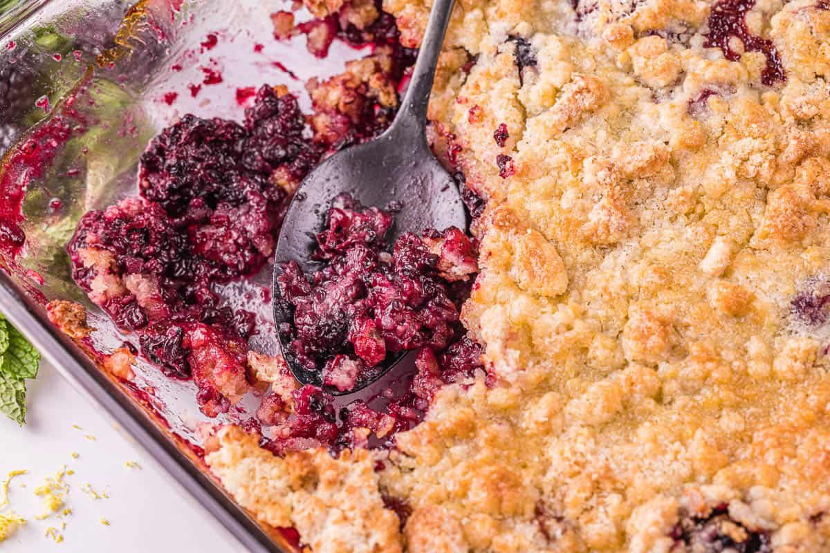 scooping blackberry cobbler out of baking dish.