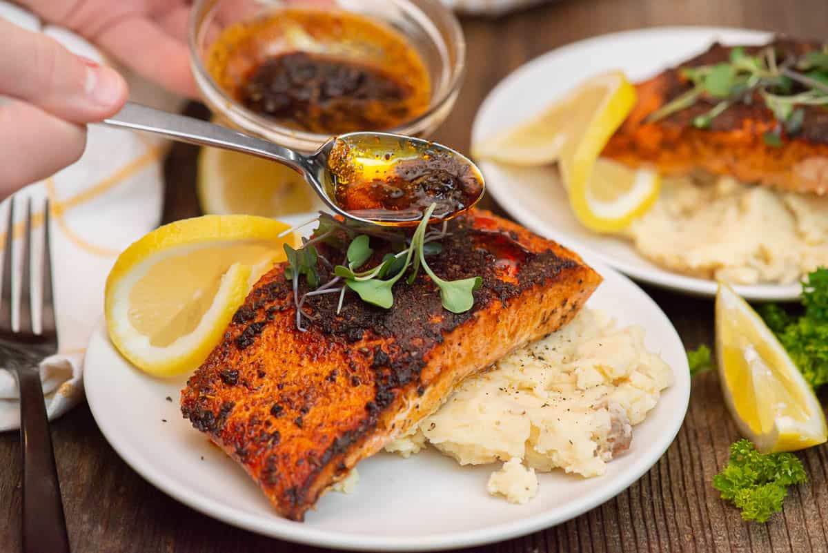 spooning flavored butter over blackened salmon.