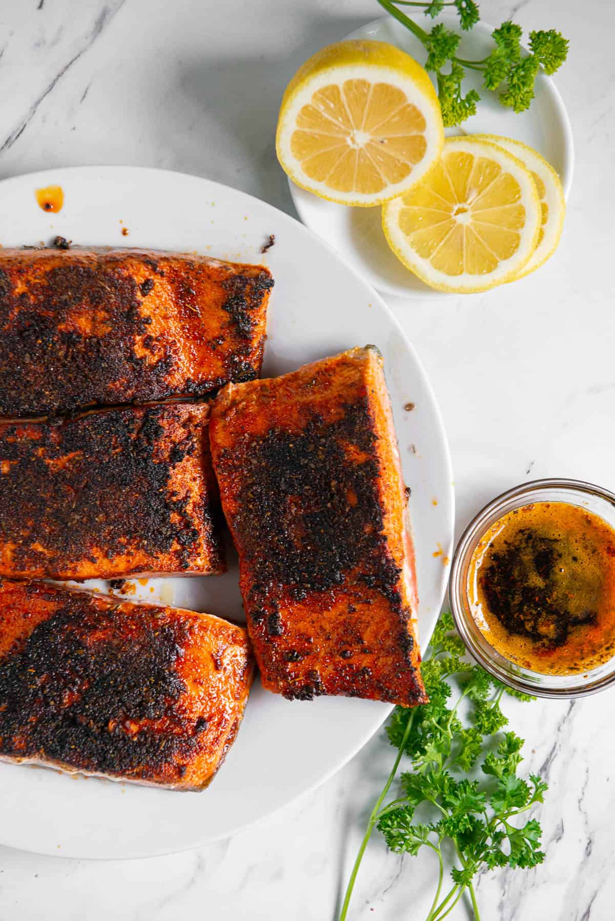 blackened salmon filets on plate with lemon and butter sauce.
