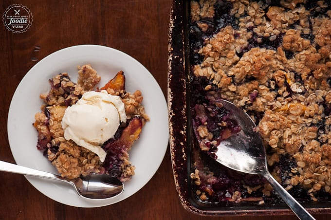 bowl of blueberry peach crisp topped with vanilla ice cream