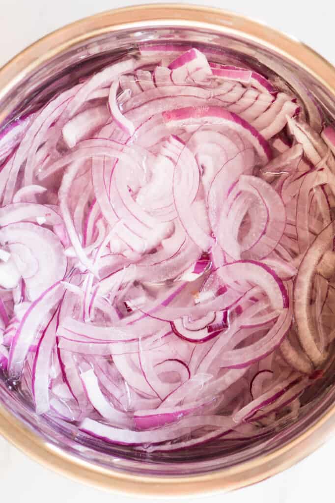 sliced red onions in bowl of water