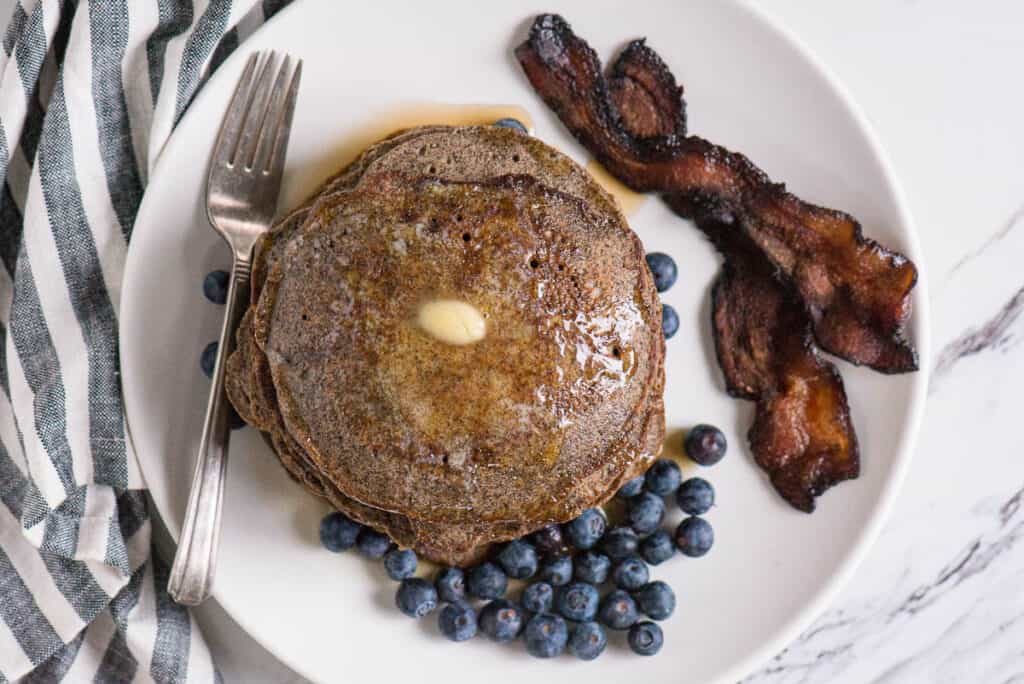 white plate with Buckwheat Pancakes, fresh blueberries, and bacon