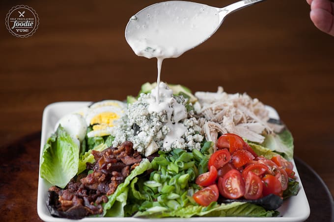 pouring bleu cheese dressing onto cobb salad