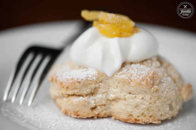 a close up of a buttermilk lemon scone with a cream topping with lemon garnish