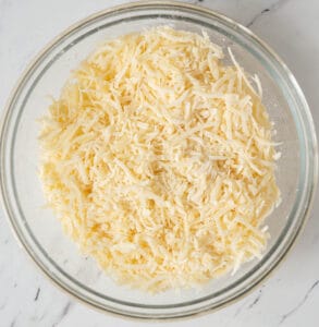 grated Swiss cheese tossed with cornstarch in glass bowl.
