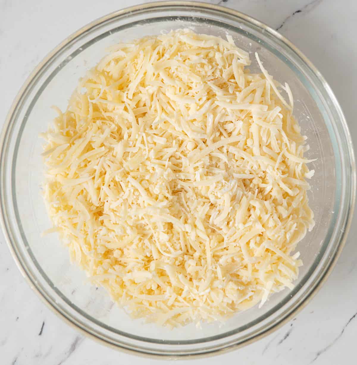 grated Swiss cheese tossed with cornstarch in glass bowl.